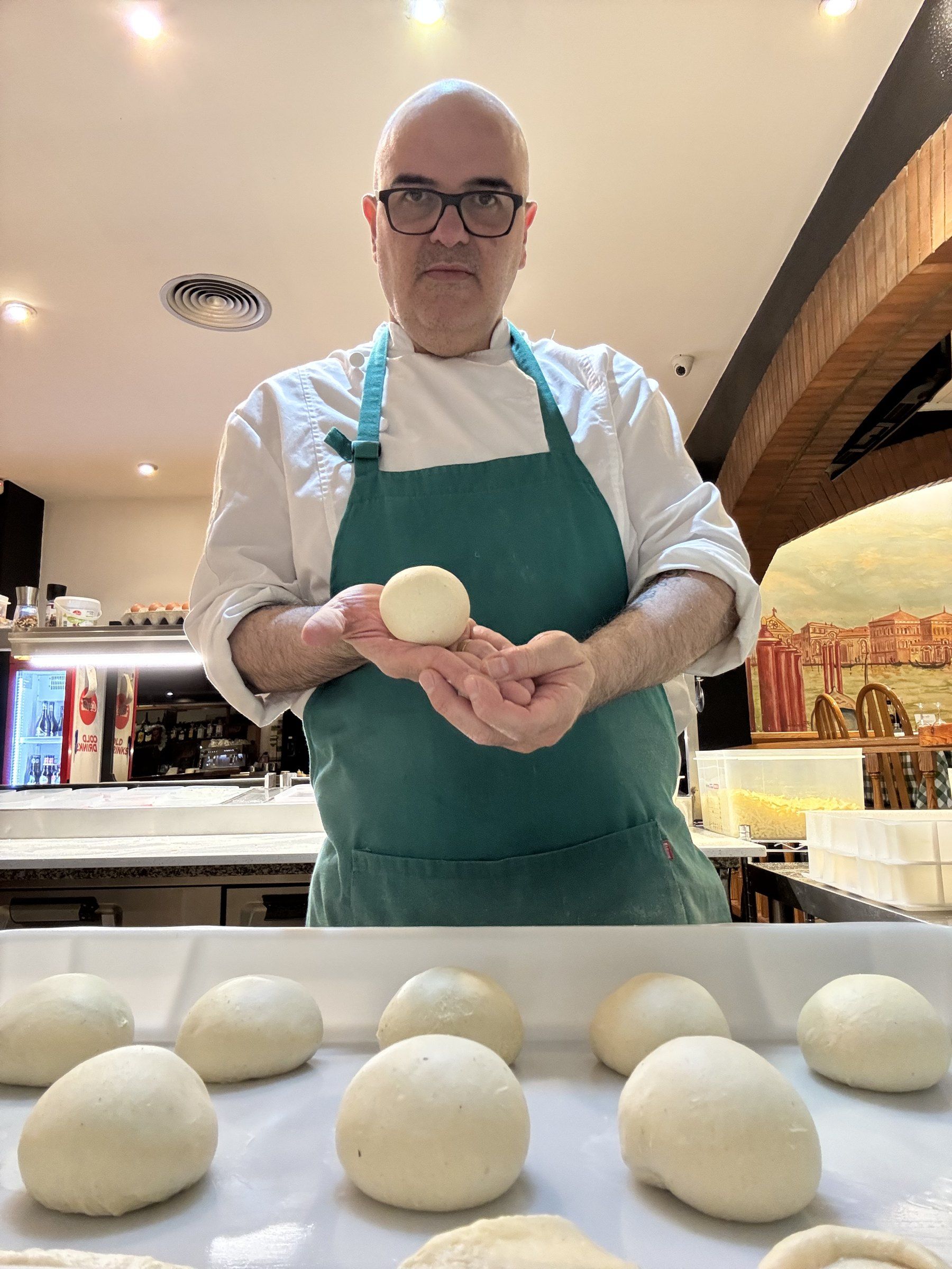 En Luiggi, amb davantal verd, ensenya una bola de massa davant de la safata