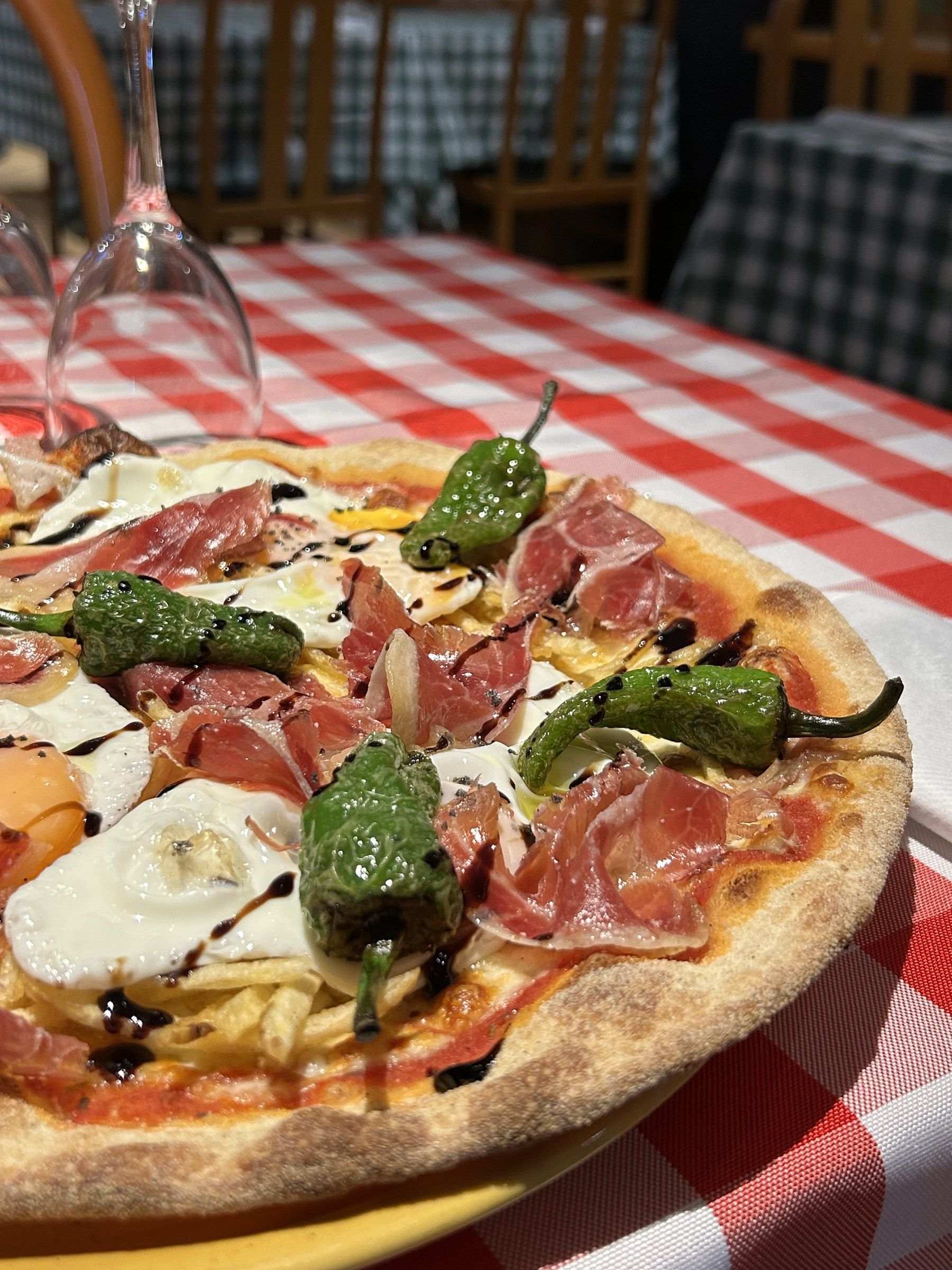 Pizza amb pernil, ous, patates palla i pebrots del Padró sobre estovalles vermelles