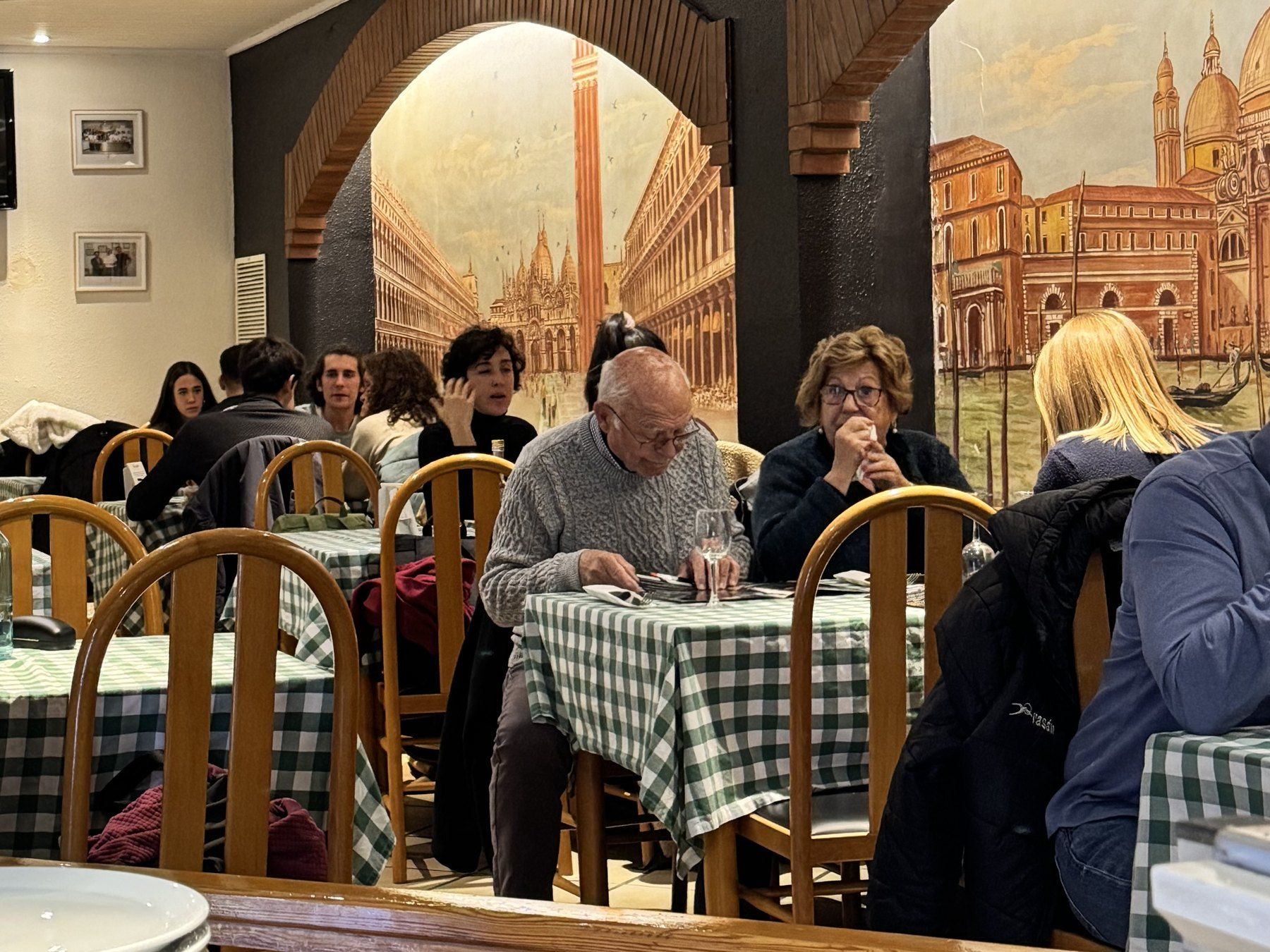 La sala de Trattoria da Luiggi plena de clients sopant, sota l'arc de maó i els murals de Venècia